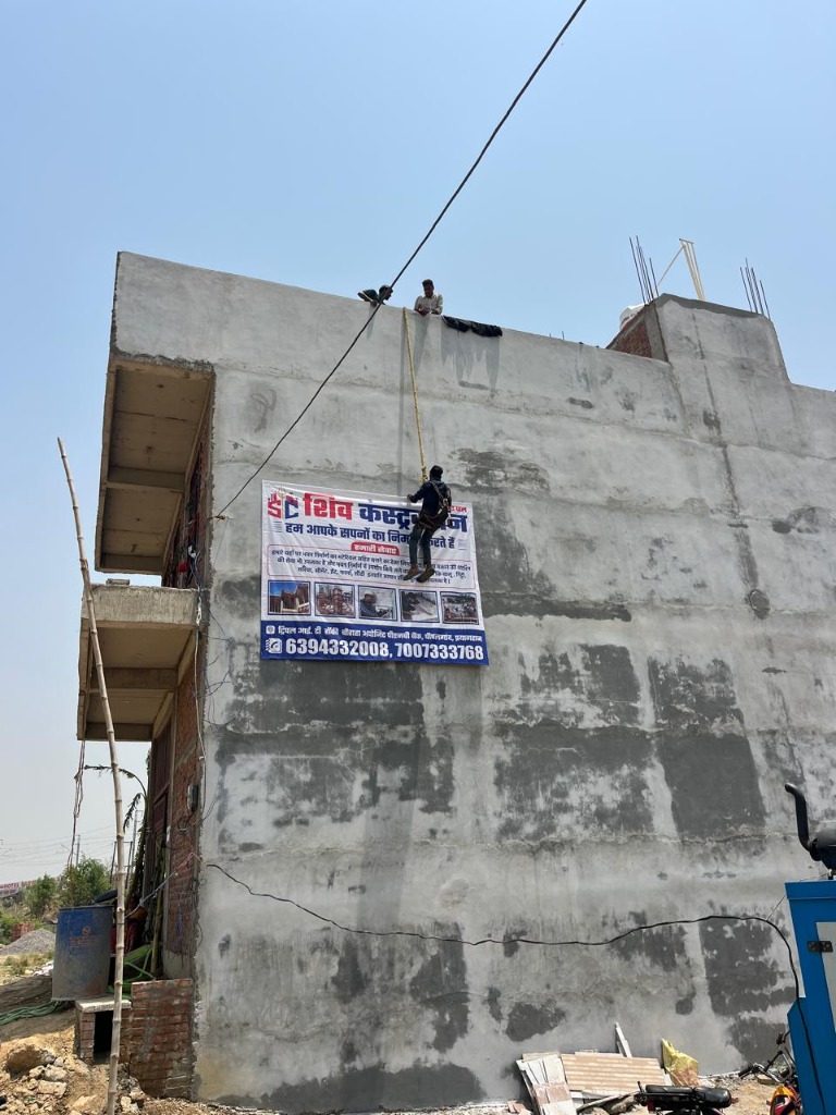Workers hanging Shiv Construction banner on concrete site structure